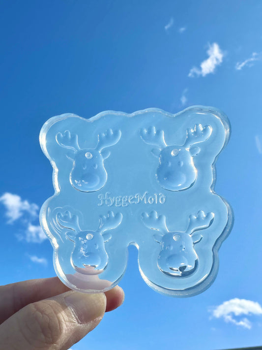 Clear silicone mold with reindeer designs held against a blue sky.